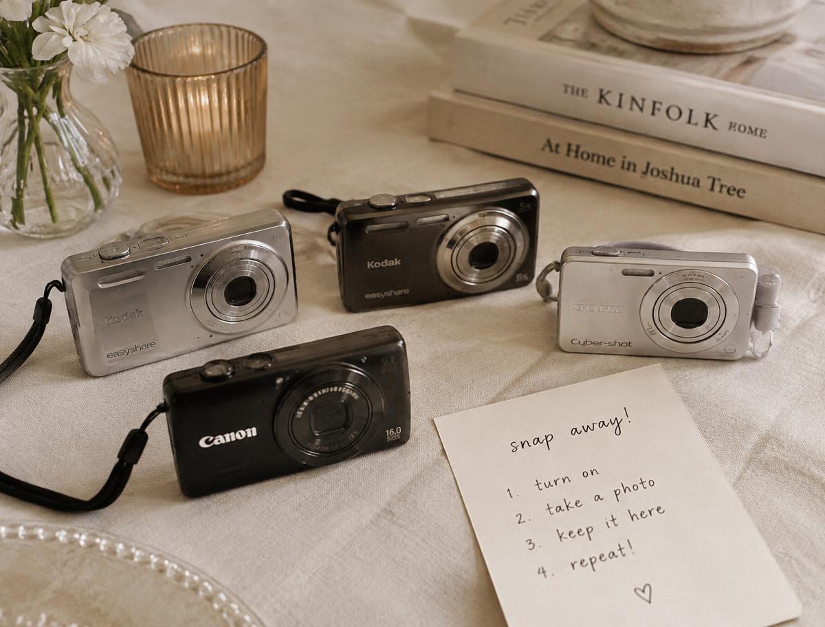 Four small digital cameras set out on an ivory linen table with an instruction card