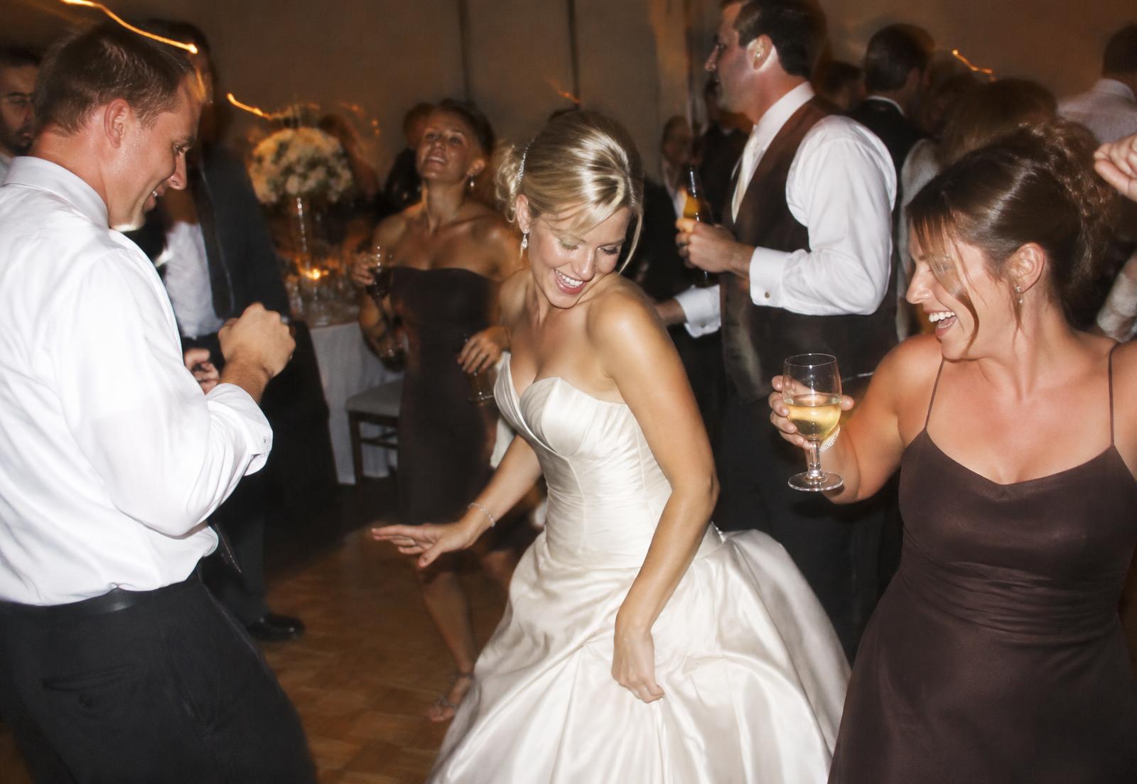 Wedding guests laughing and dancing at a reception, lit by camera flash