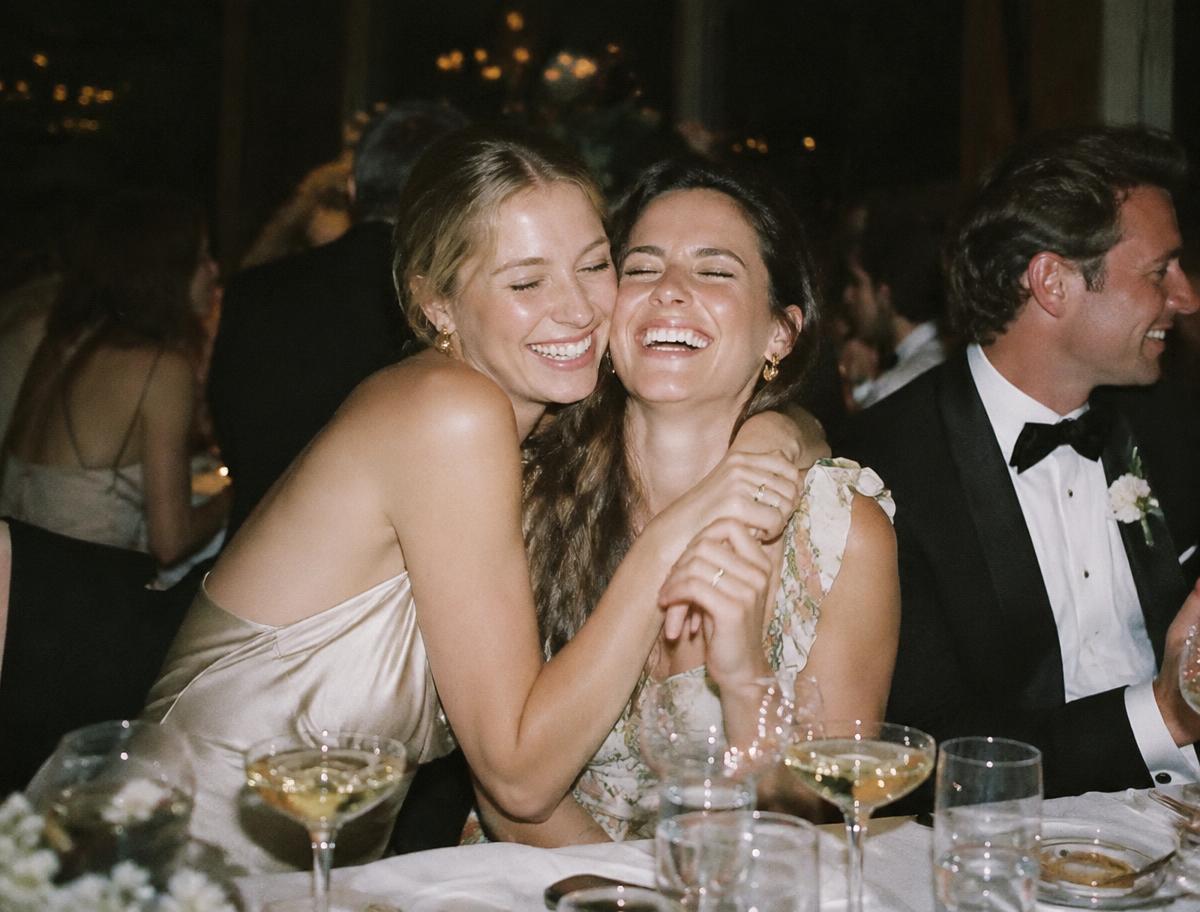 Two friends laughing together at a wedding reception table